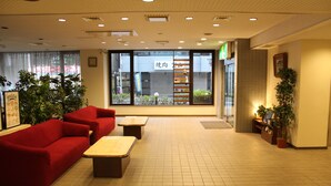 Een ruime lobby met een rode bank, houten tafels, potplanten en grote ramen met uitzicht op buiten.