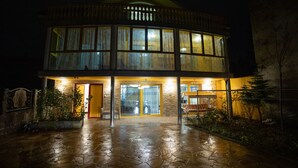 Un bâtiment à deux étages, doté d’une entrée pavée de pierres, de grandes fenêtres et d’un espace extérieur couvert aménagé en coin salon.