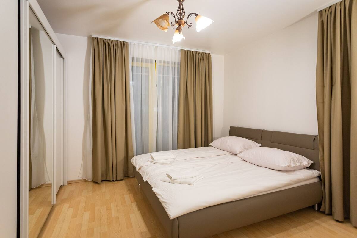 Une chambre à coucher avec un grand lit, un lustre et des rideaux de couleur beige.
