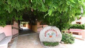 A stone sign with the inscription "RESIDENZA LE DUELPALMI" surrounded by greenery and a paved pathway. - Le Due Palme Residences - Four-room apartment 3 (Villasimius)