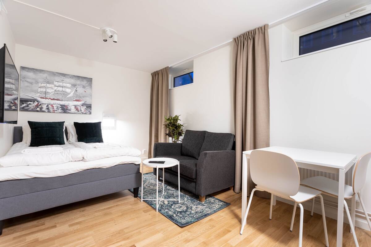 Un dormitorio moderno con una cama, un sofá gris, un escritorio blanco y una mesita pequeña.