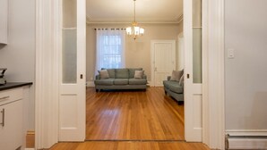 A spacious living room with a wooden floor, a green sofa, and a white door.
