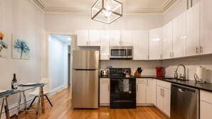 A modern kitchen with white cabinets, stainless steel appliances, and a wooden floor.