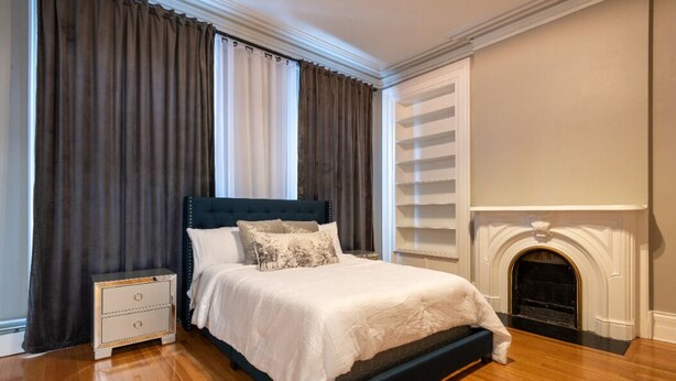 A bedroom with a bed, a nightstand, a fireplace, and curtains.