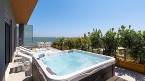 Um terraço no telhado com banheira de hidromassagem, área de estar ao ar livre e vista para o mar.
