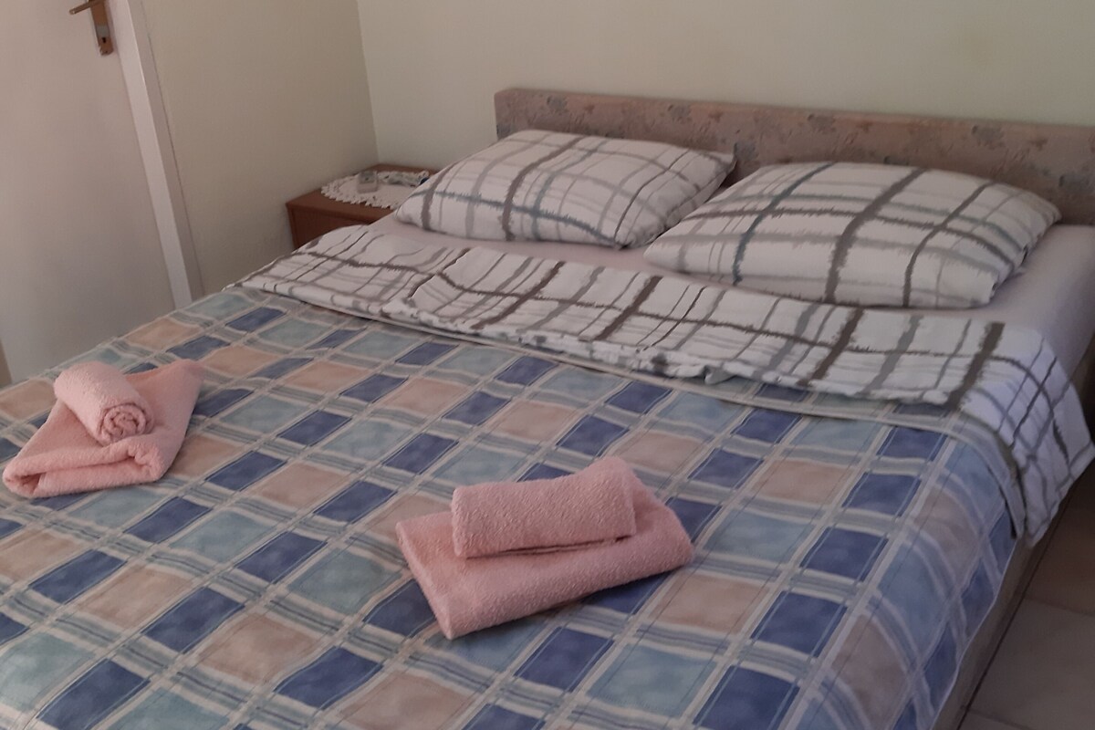 A neatly made bed with a checkered bedspread and two pink towels folded on it.
