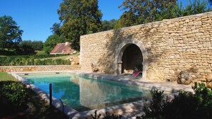 Un bâtiment en pierre doté d’une piscine, entouré de verdure et d’arbres.