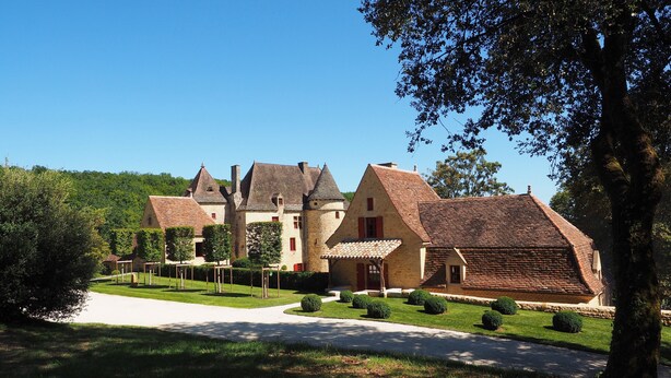 Un bâtiment traditionnel en pierre, doté de nombreuses cheminées, avec une pelouse bien entretenue et un ciel dégagé.
