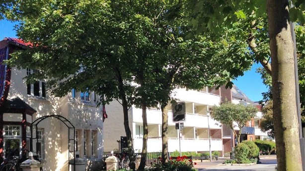 A street with a sidewalk, trees, and a building with a red roof. - Spalthoff 18, Germany (Sylt)