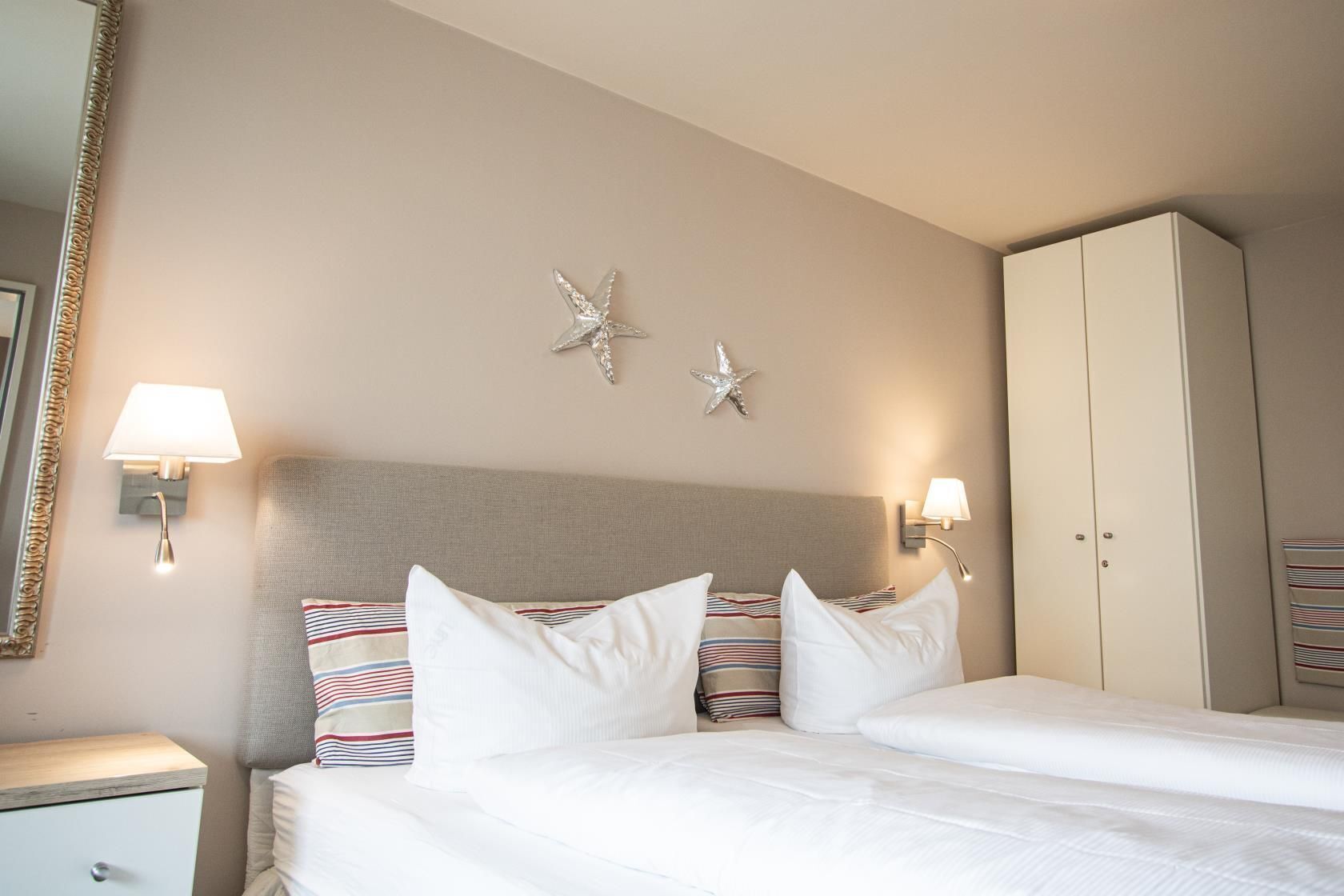 Ett hotellrum med en säng, två vägglampor, en garderob och två sjöstjärnedekorationer på väggen.