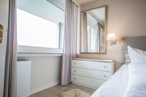 Hotellihuone, jossa on sänky, lipasto, peili ja ikkuna, jossa on verhot.