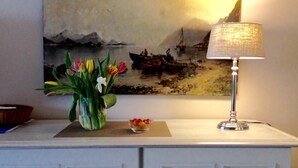 A painting of a seascape with boats, a vase of tulips, a bowl of beads, and a lamp on a white cabinet. - Spalthoff 18, Germany (Sylt)
