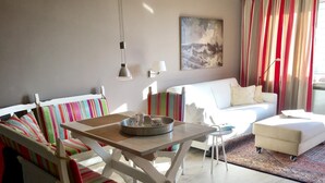 A modern living room with a striped sofa, a white couch, a small table with a tray, and a painting on the wall. - Spalthoff 18, Germany (Sylt)