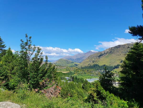 A mountainous landscape with a valley, dense greenery, and a clear blue sky. - Entire 2 bedroom detached chalet, in private woodland with valley views. (Arthurs Point)