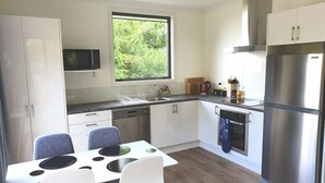 A modern kitchen with white cabinets, a stainless steel refrigerator, and a window overlooking greenery. - Entire 2 bedroom detached chalet, in private woodland with valley views. (Arthurs Point)