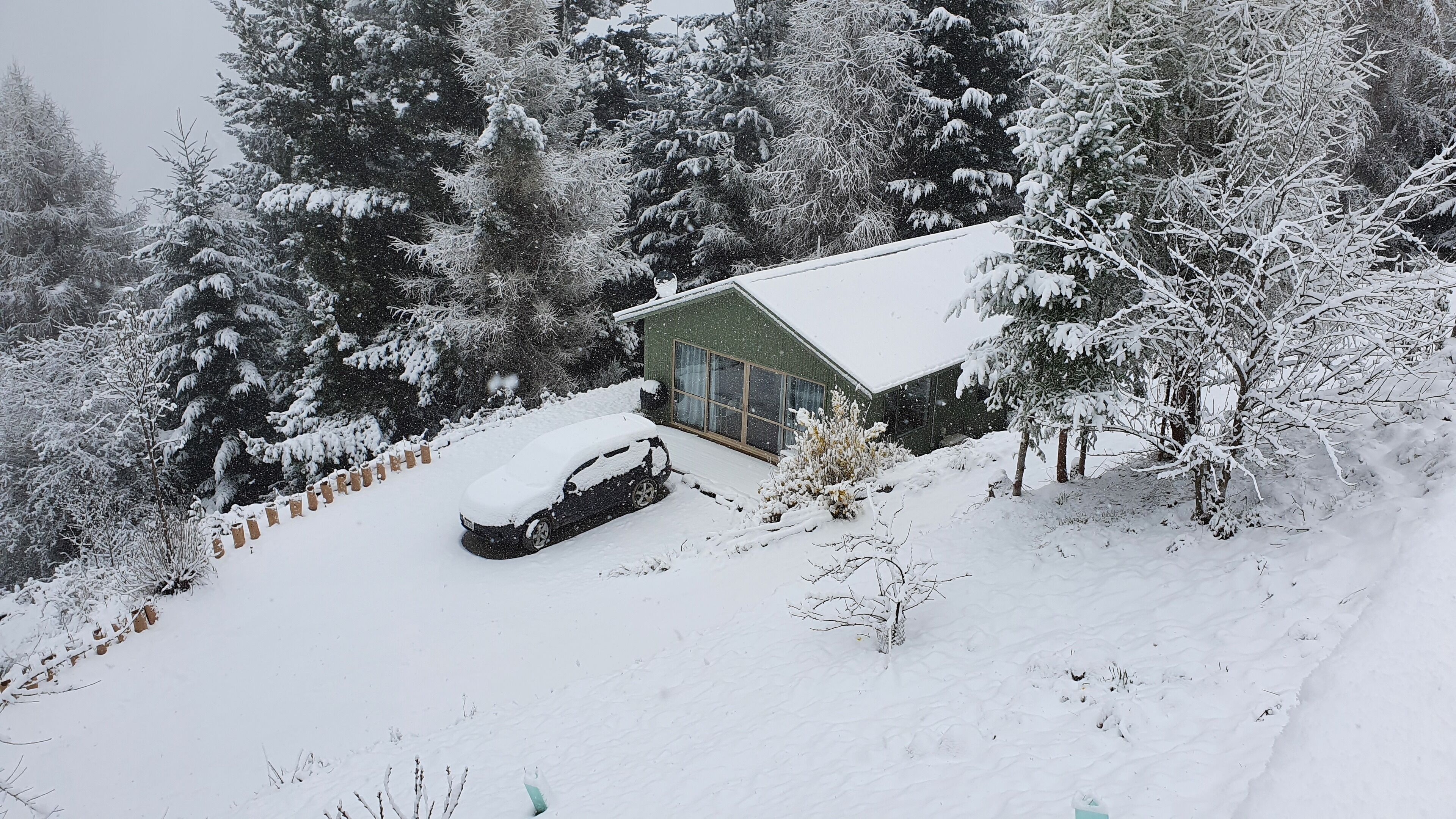 A snow-covered landscape with a house and a car parked in front.