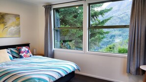 A bedroom with a large window, a bed with striped bedding, a globe on a side table, and a painting on the wall. - Entire 2 bedroom detached chalet, in private woodland with valley views. (Arthurs Point)