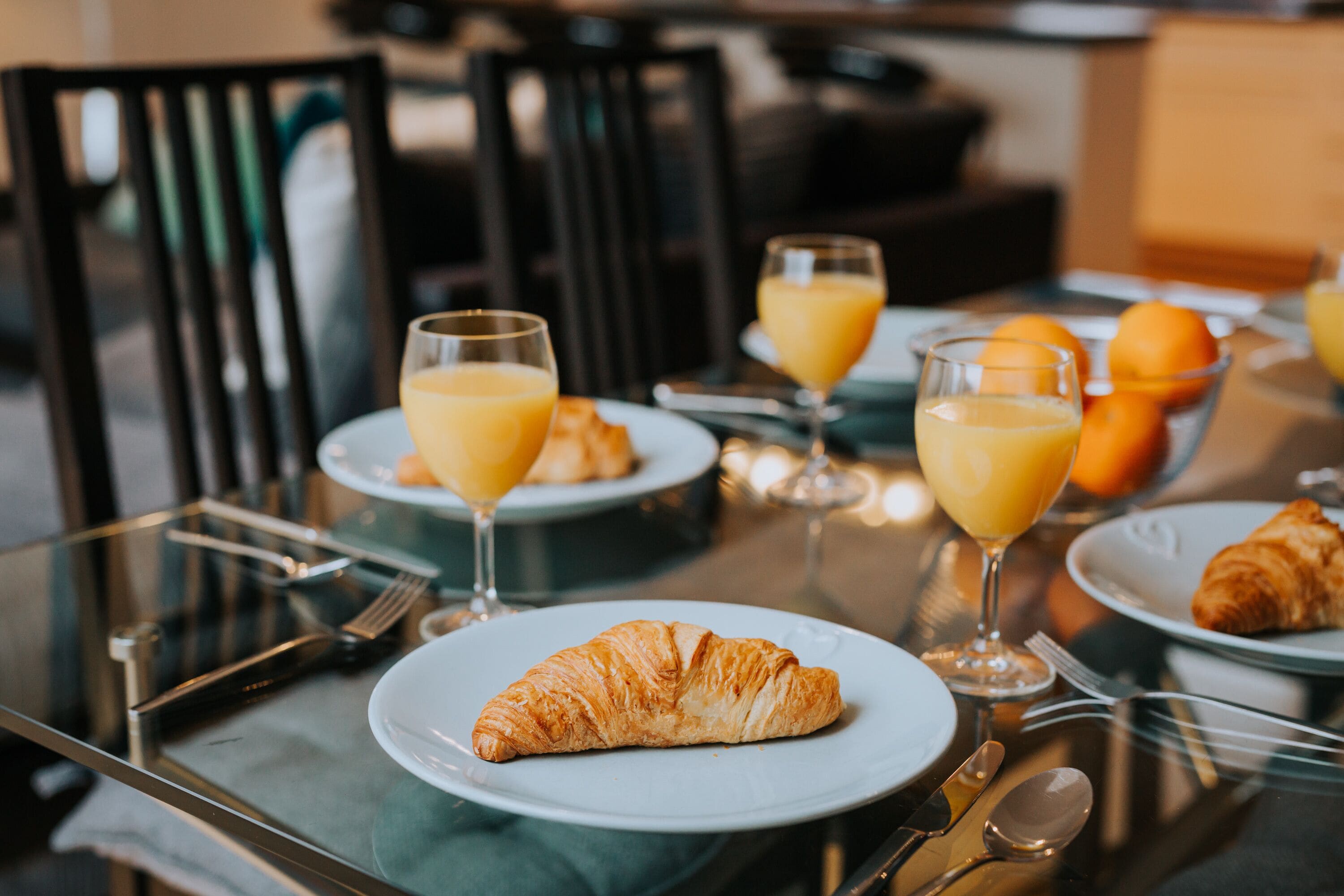 Disposição para o café da manhã com croissants, suco de laranja e um croissant em um prato.