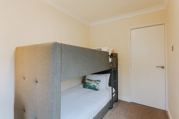 A single bed with a grey headboard, a white pillow, and a teal pillow with a beach scene. - The Penthouse (Newquay)