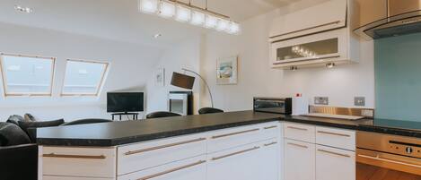 A modern kitchen with white cabinets, a black countertop, stainless steel appliances, and a ceiling light fixture.