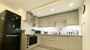 Une cuisine moderne avec un réfrigérateur noir, des appareils en acier inoxydable et des meubles de couleur claire.