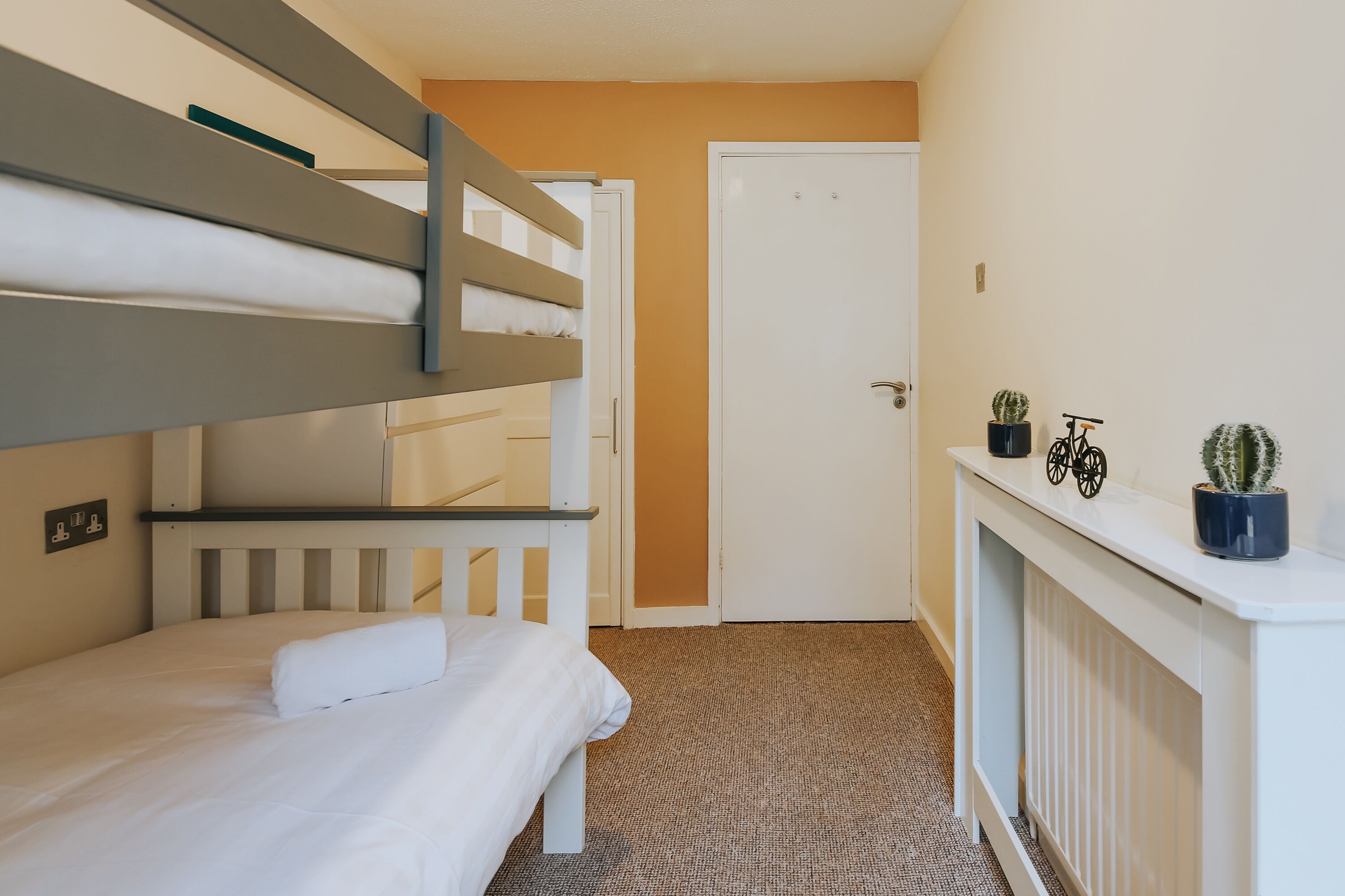 Una cama litera con ropa de cama blanca y una pequeña mesa con una planta en maceta.