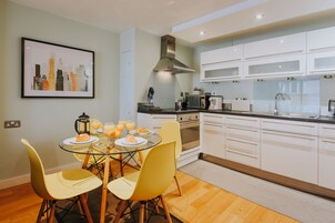 A modern kitchen with white cabinets, a stainless steel range hood, and a dining area with yellow chairs and a glass table.