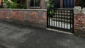 Un bâtiment en briques de deux étages, doté d’un portail noir, d’un balcon et d’une porte avec une fenêtre.