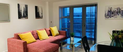 Una sala de estar moderna con un sofá rojo, cojines amarillos, una mesa de centro de vidrio y vistas amplias a través de grandes ventanales.