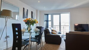 A modern living room with a glass dining table, black chairs, a sofa, and a TV. - Clarence Court (Newcastle-upon-Tyne)