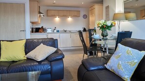 A modern living room with a black leather sofa, a glass coffee table, and a dining area with a glass table and chairs. - Clarence Court (Newcastle-upon-Tyne)