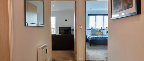 Un pasillo que conduce a un dormitorio con cama, televisor y ventana.
