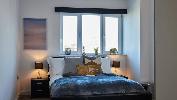A bedroom with a bed, two bedside tables, a window, and a wall-mounted artwork. - Clarence Court (Newcastle-upon-Tyne)