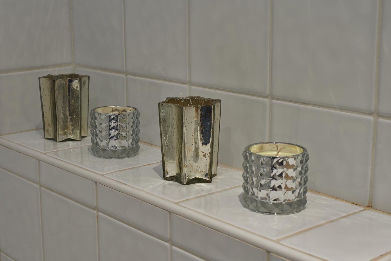 Three glass candle holders on a white tiled shelf.