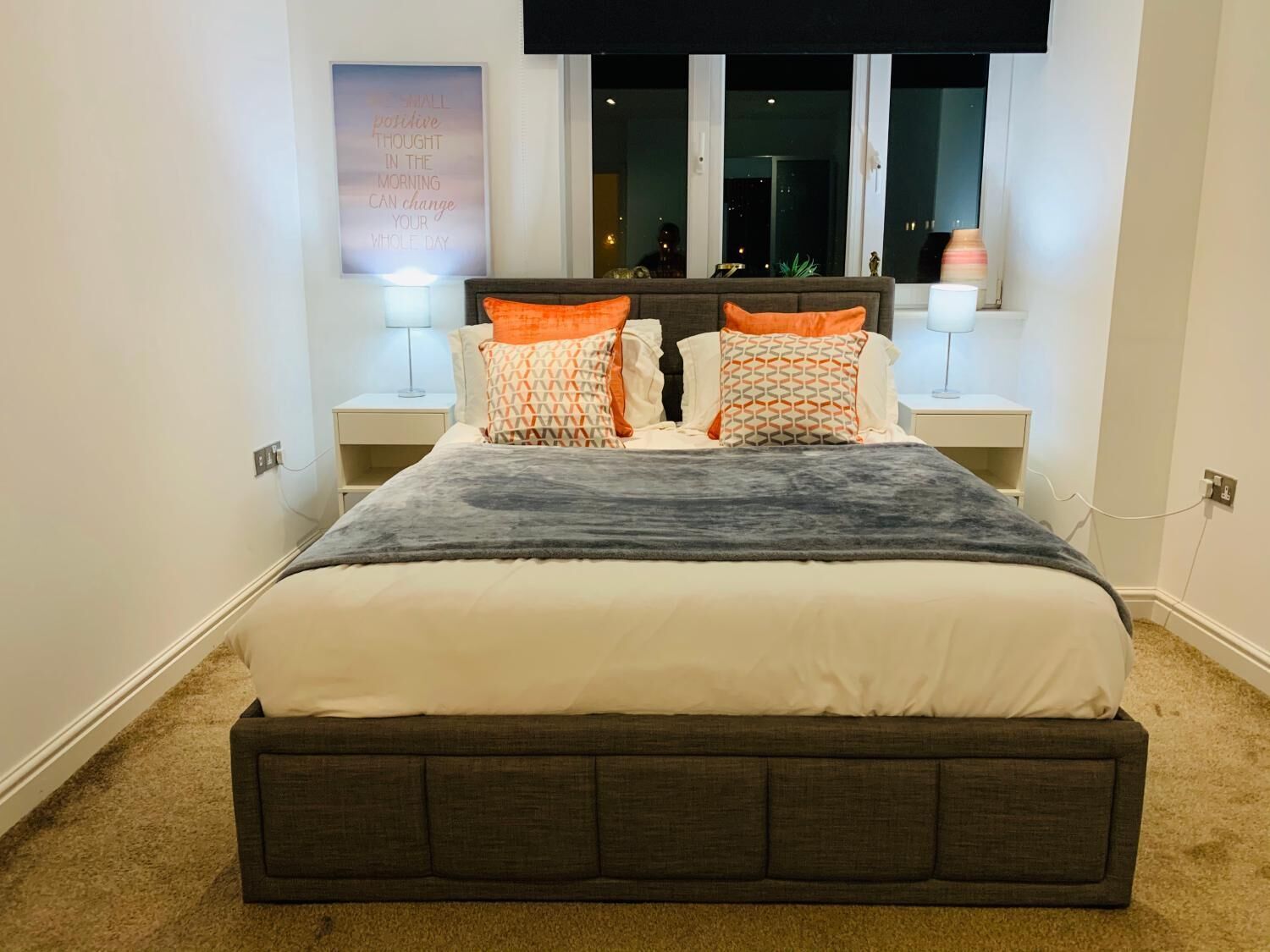 A neatly arranged bedroom with a large bed, two bedside tables, and a motivational poster on the wall.