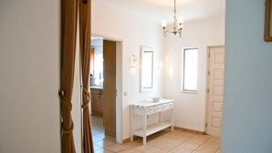 Un couloir propre et bien éclairé, avec une console blanche, un miroir et une porte donnant sur un espace cuisine.