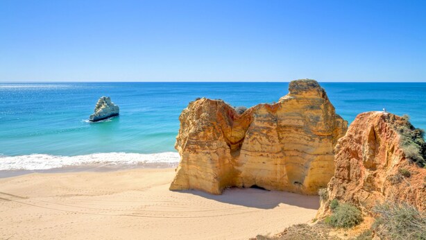 Une plage bordée de grandes formations rocheuses, sous un ciel bleu et dégagé.