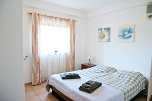 A bedroom with a bed, curtains, a nightstand, and two wall-mounted flower paintings. - Casa Linda, comfortable villa with private pool (Porches)