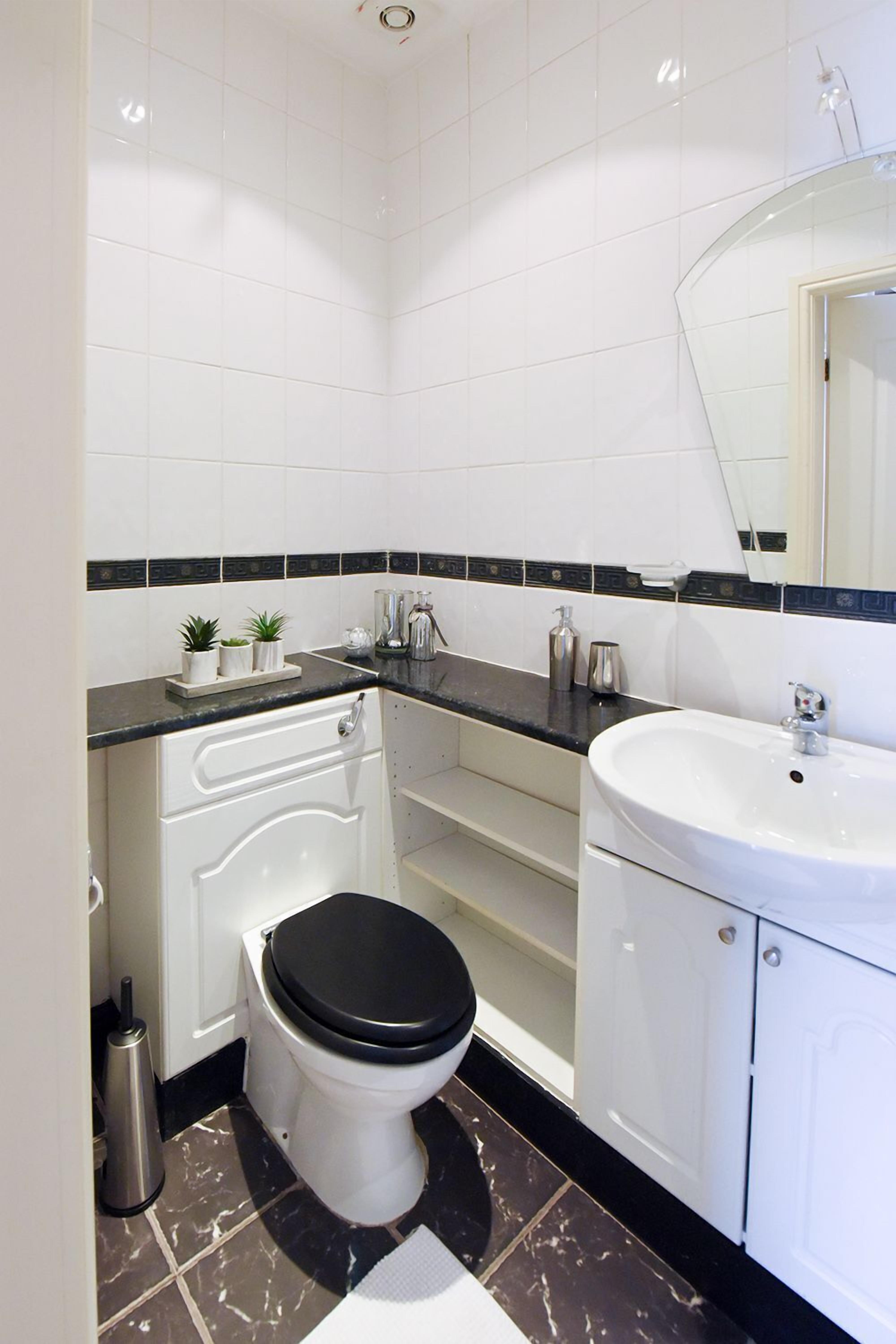 Un baño moderno con azulejos blancos, encimera negra, lavamanos blanco y inodoro negro.