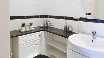 Un baño moderno con azulejos blancos, encimera negra, lavamanos blanco y inodoro negro.