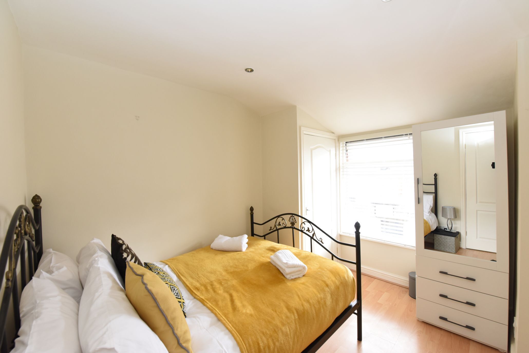 A bedroom with a bed, a dresser, and a window with blinds.