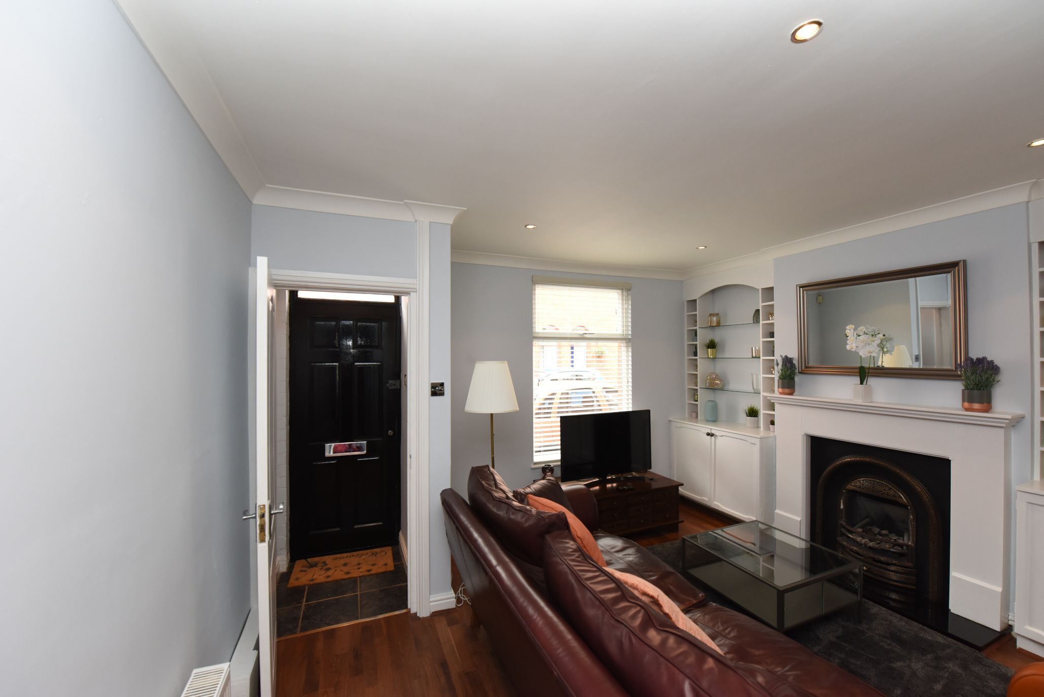 A living room with a brown leather sofa, a glass coffee table, a fireplace, and a television.