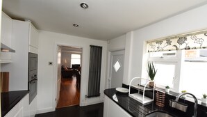 A modern kitchen with white cabinetry, a black countertop, and a stainless steel sink. - Honeysuckle House (Chester)