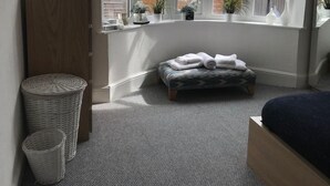 A bedroom with a large window, a bed, a small bench, a wooden cabinet, and two baskets. - Eastville Court (Rhyl)