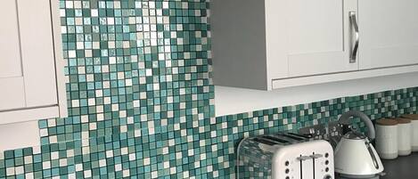 A kitchen with a black countertop, white cabinets, a tiled backsplash, and a stainless steel range hood.