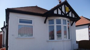 A white house with a black timber-framed gable, a bay window, and potted plants. - Eastville Court (Rhyl)