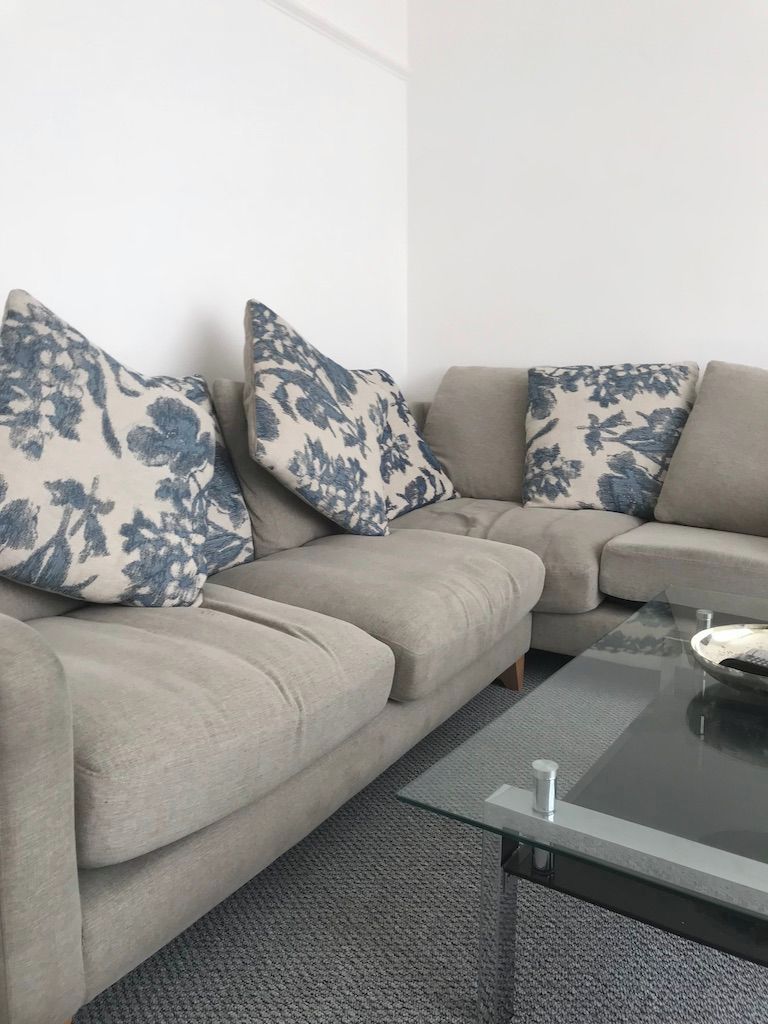 A modern living room with a sectional sofa, a glass coffee table, and floral-patterned cushions.