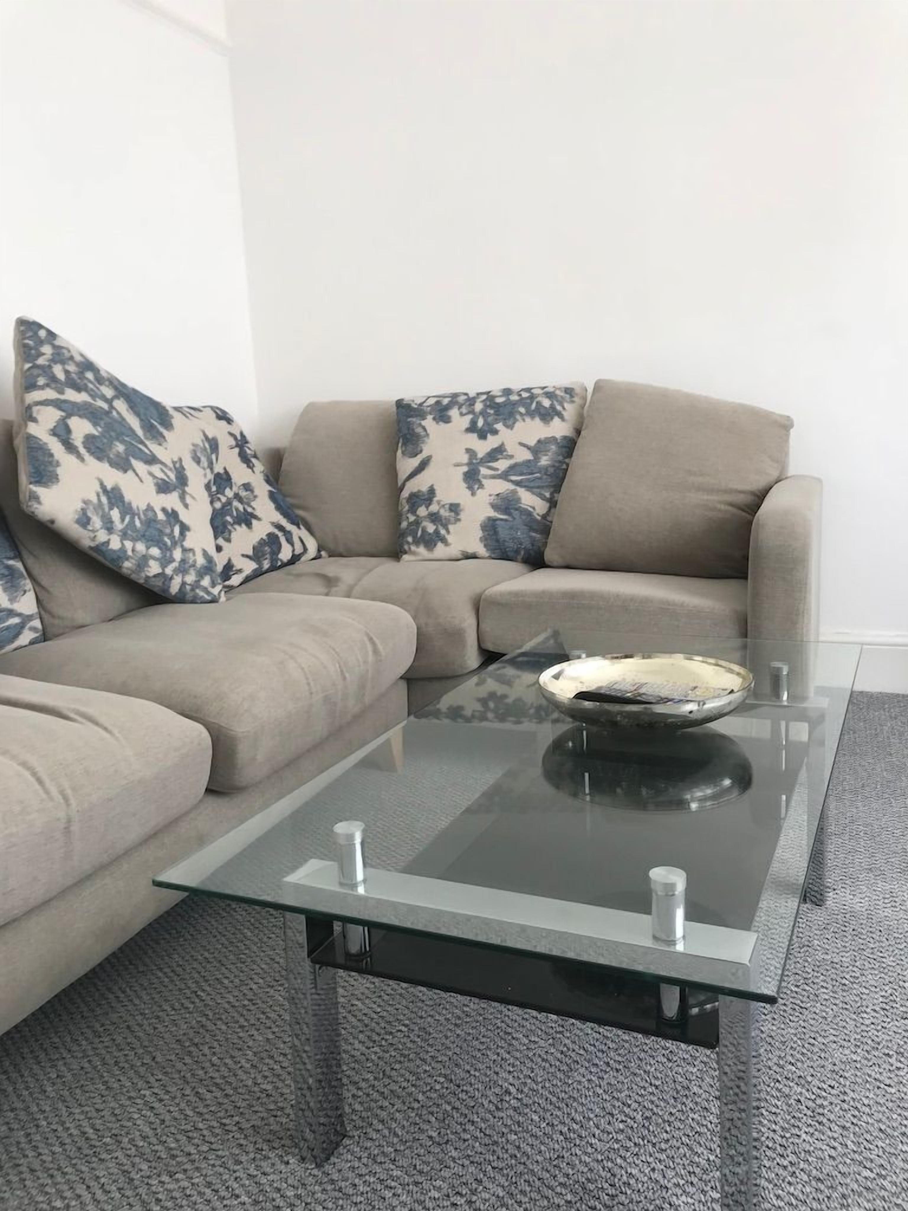Ein Wohnzimmer mit einem Glastisch, einem beigen Sofa und Kissen mit Blumenmuster.