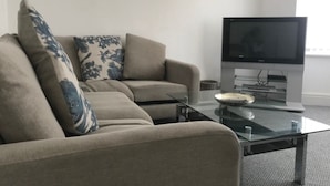A living room with a beige sofa, a glass coffee table, and a flat-screen TV. - Eastville Court (Rhyl)