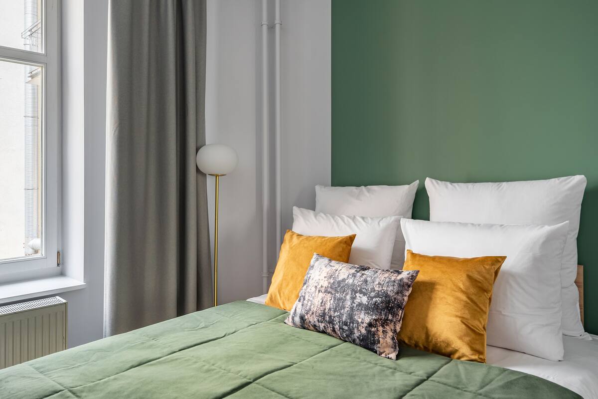 A bedroom with a green bedspread, white pillows, and a mustard-colored pillow.
